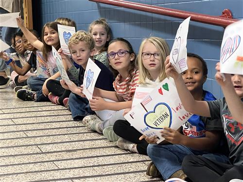 kids along walls at Madison Elementary holding up thank you signs to veterans